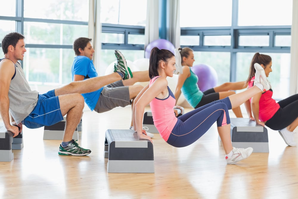 Full length side view of instructor with fitness class performing step aerobics exercise in gym